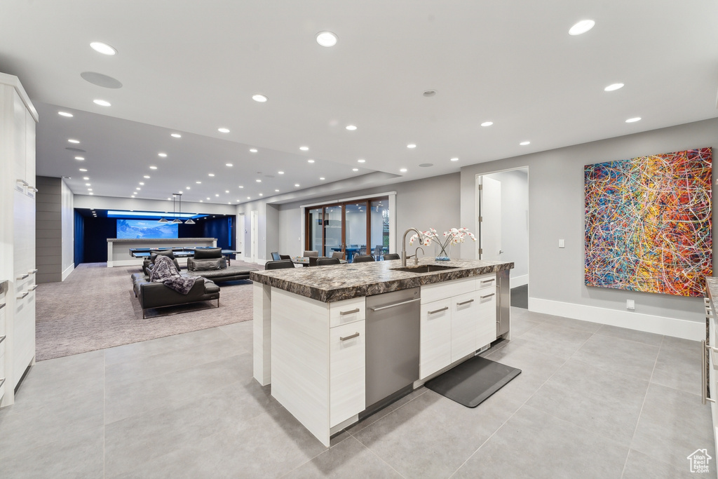 Kitchen with stainless steel dishwasher, a kitchen island with sink, white cabinetry, light tile patterned floors, and sink