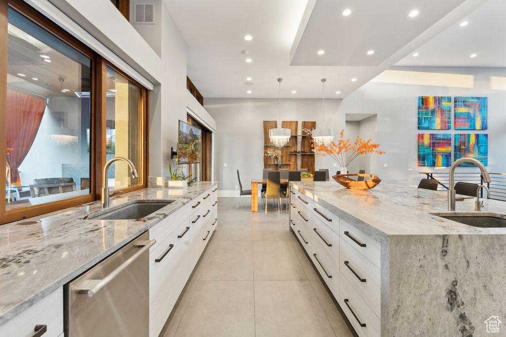 Kitchen featuring sink, light stone counters, pendant lighting, and white cabinets