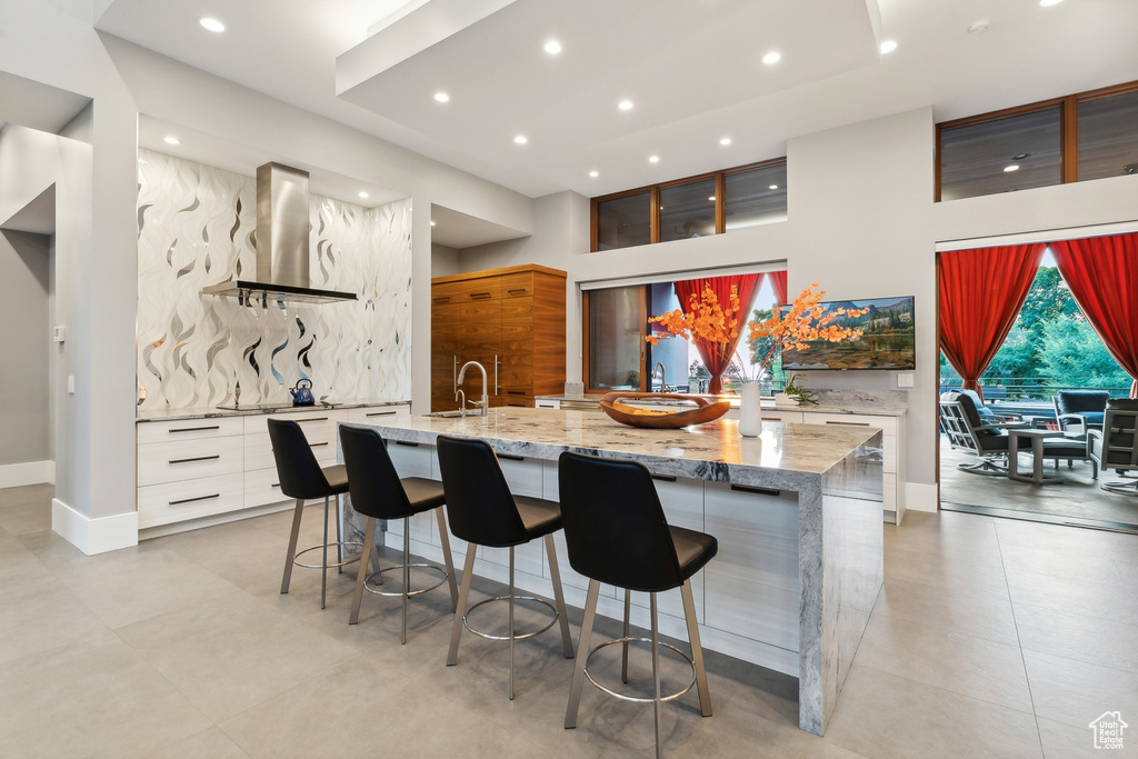 Kitchen with decorative backsplash, light stone counters, white cabinets, light tile patterned floors, and exhaust hood