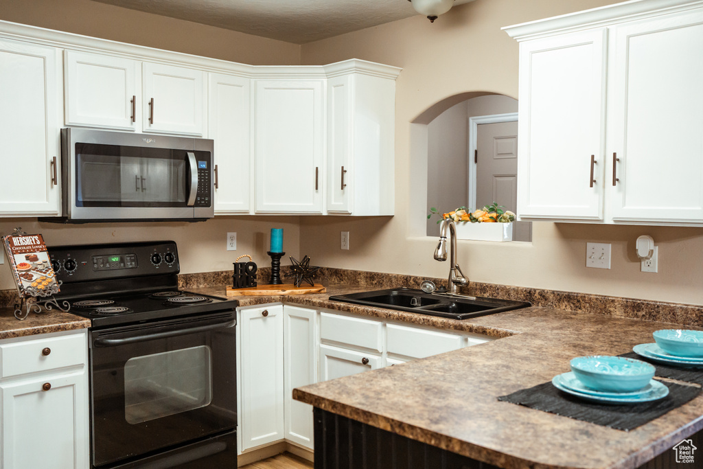 Kitchen featuring white cabinets, electric range, and sink