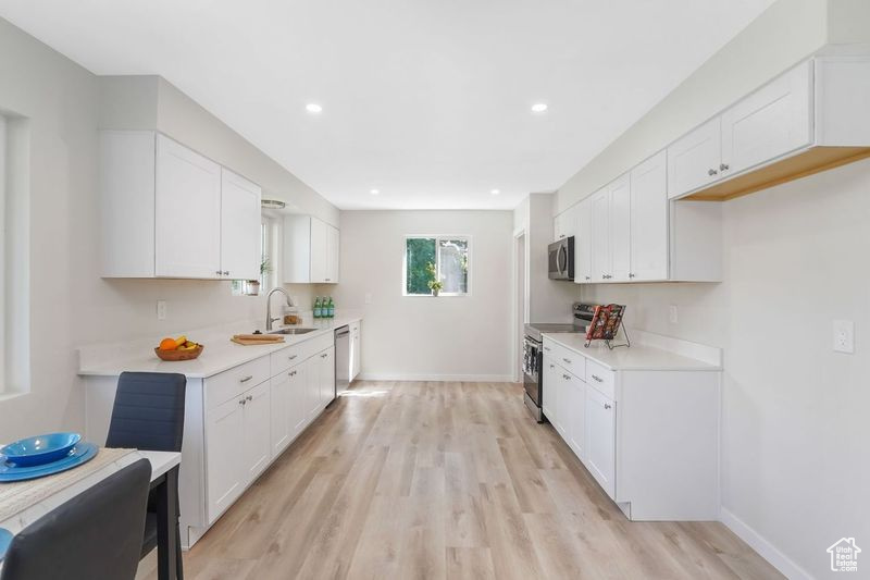 Kitchen with stainless steel appliances, white cabinetry, and light hardwood / wood-style flooring