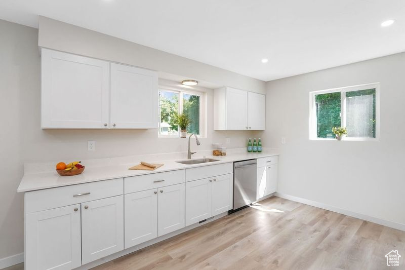 Kitchen with sink, white cabinets, stainless steel dishwasher, and light wood-type flooring