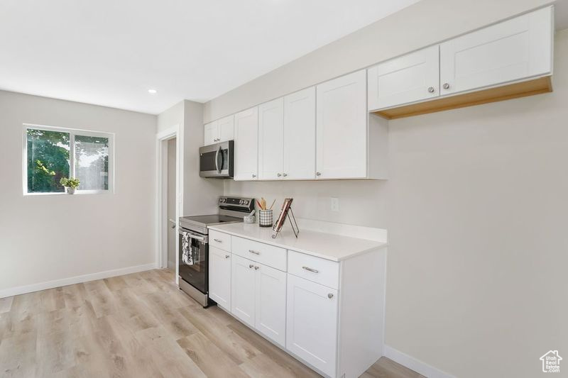 Kitchen with appliances with stainless steel finishes, light hardwood / wood-style flooring, and white cabinetry