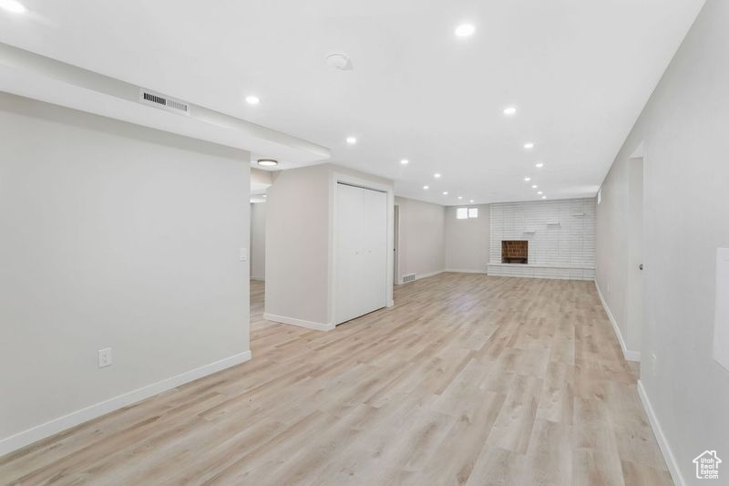 Basement featuring light wood-type flooring and a brick fireplace