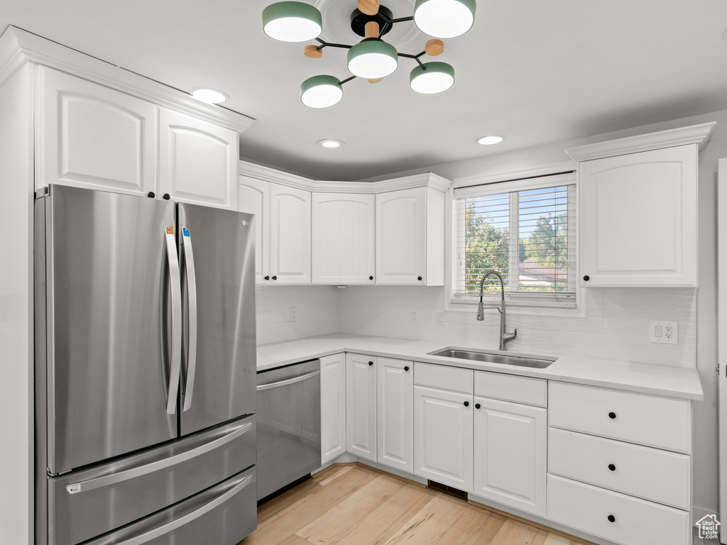 Kitchen with sink, decorative backsplash, light hardwood / wood-style floors, stainless steel appliances, and white cabinets