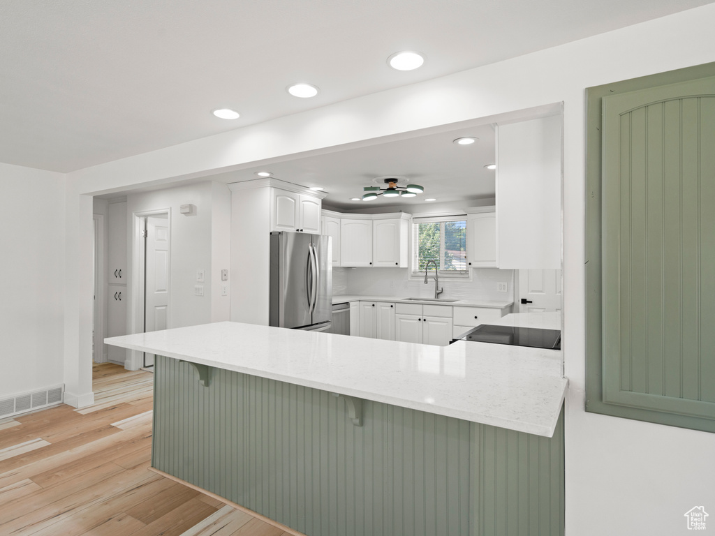 Kitchen featuring light wood-type flooring, tasteful backsplash, white cabinets, stainless steel refrigerator, and a breakfast bar area