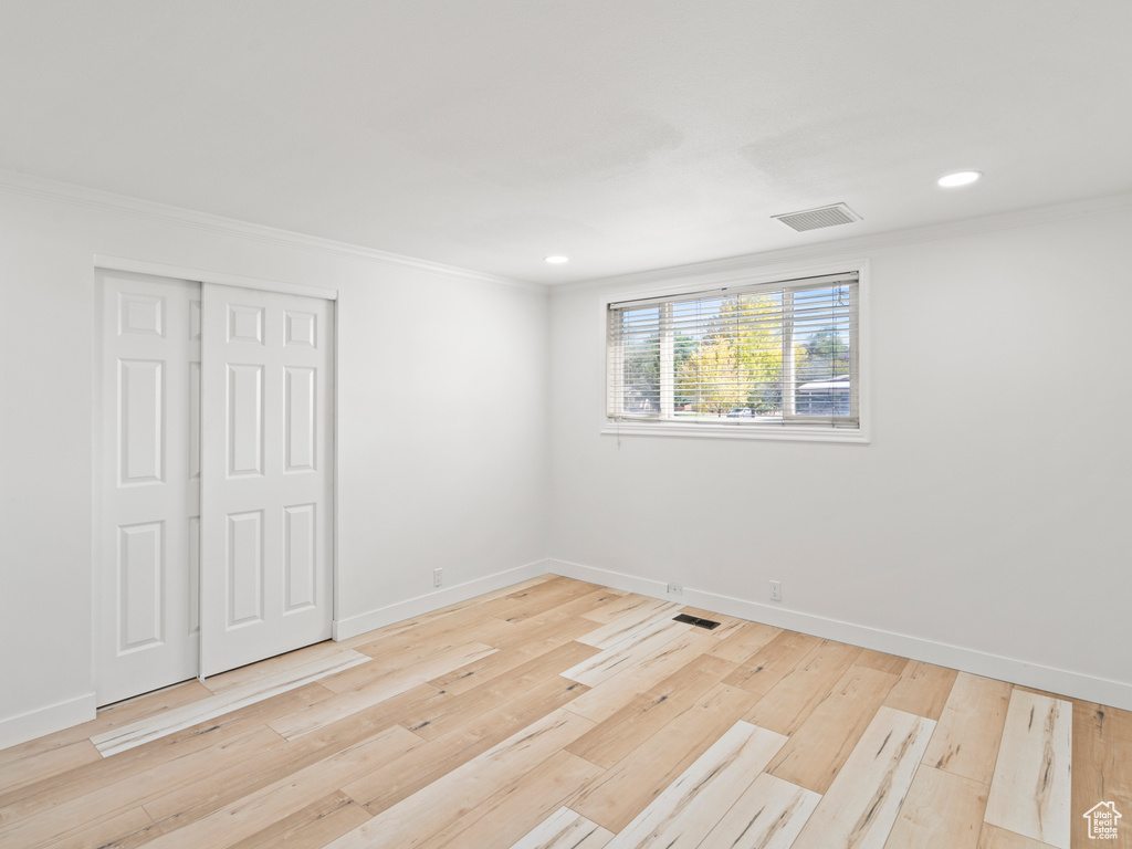 Unfurnished bedroom featuring light hardwood / wood-style floors, ornamental molding, and a closet