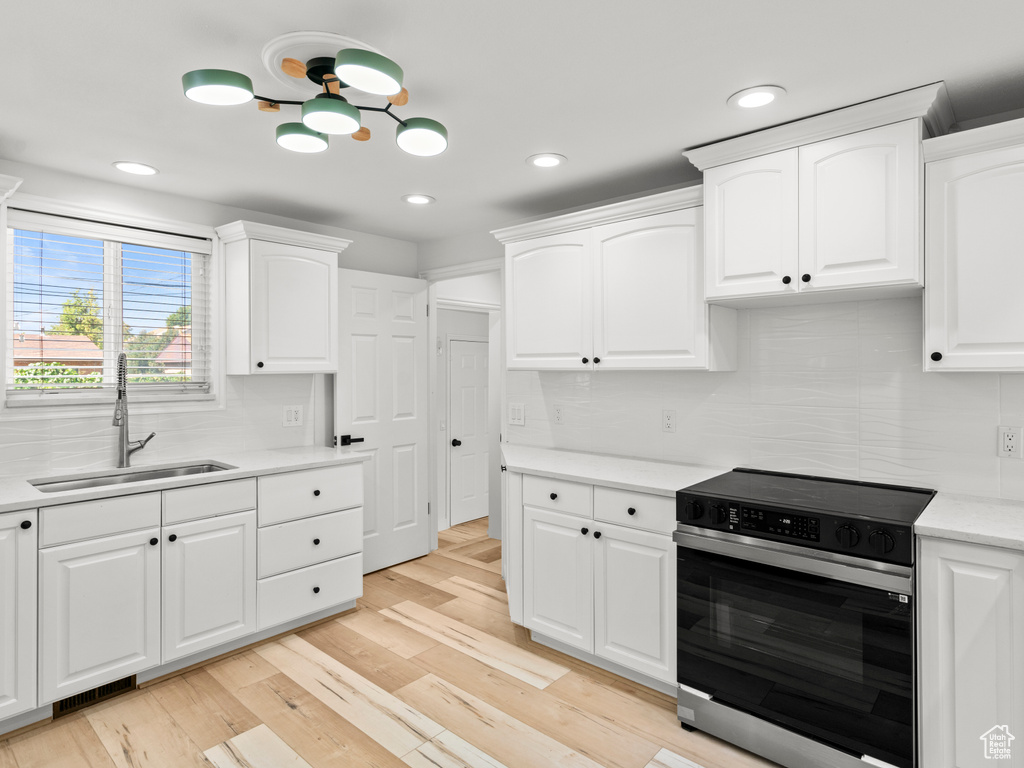 Kitchen with stainless steel range with electric stovetop, light wood-type flooring, sink, and white cabinets