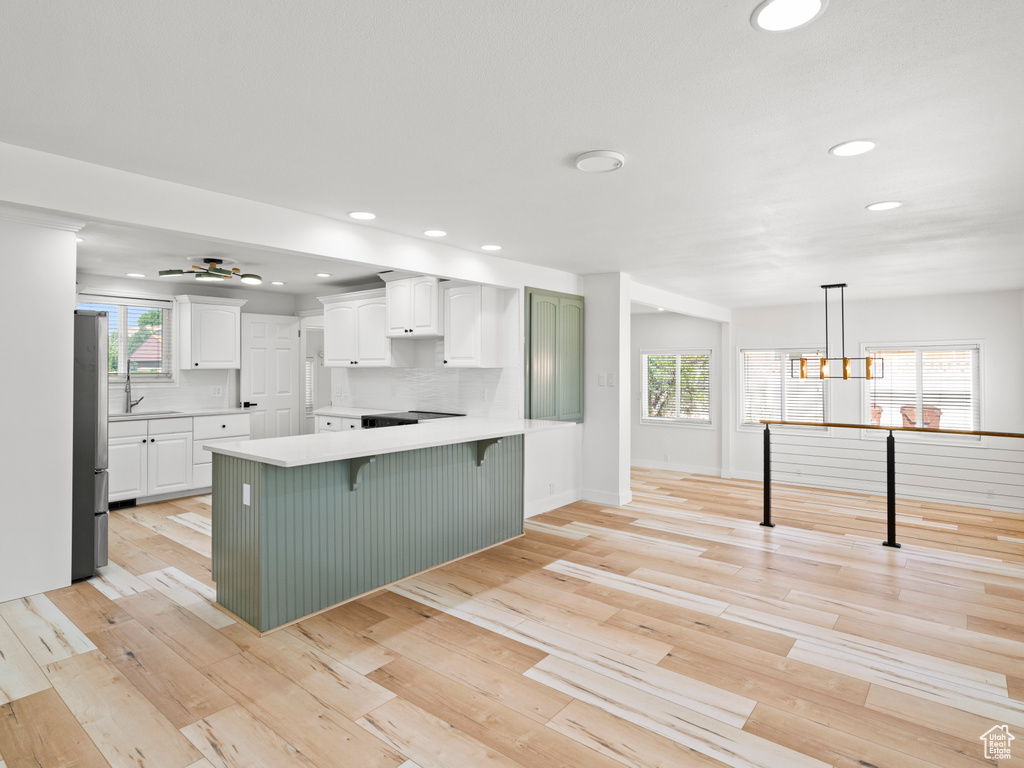 Kitchen featuring white cabinets, hanging light fixtures, a kitchen breakfast bar, and a wealth of natural light