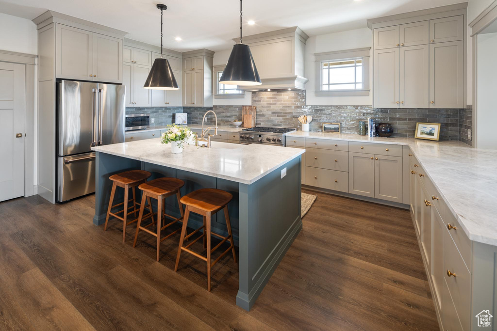 Kitchen with an island with sink, high quality appliances, dark hardwood / wood-style floors, tasteful backsplash, and pendant lighting