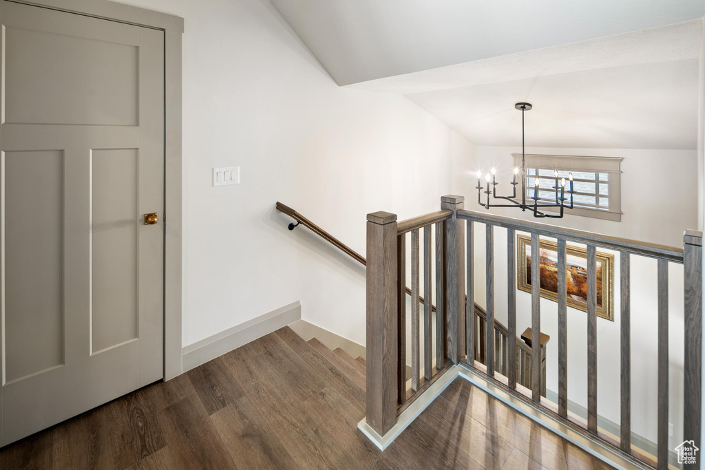 Staircase with lofted ceiling, an inviting chandelier, and wood-type flooring