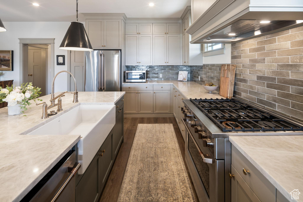 Kitchen with decorative backsplash, premium range hood, hanging light fixtures, gray cabinetry, and premium appliances