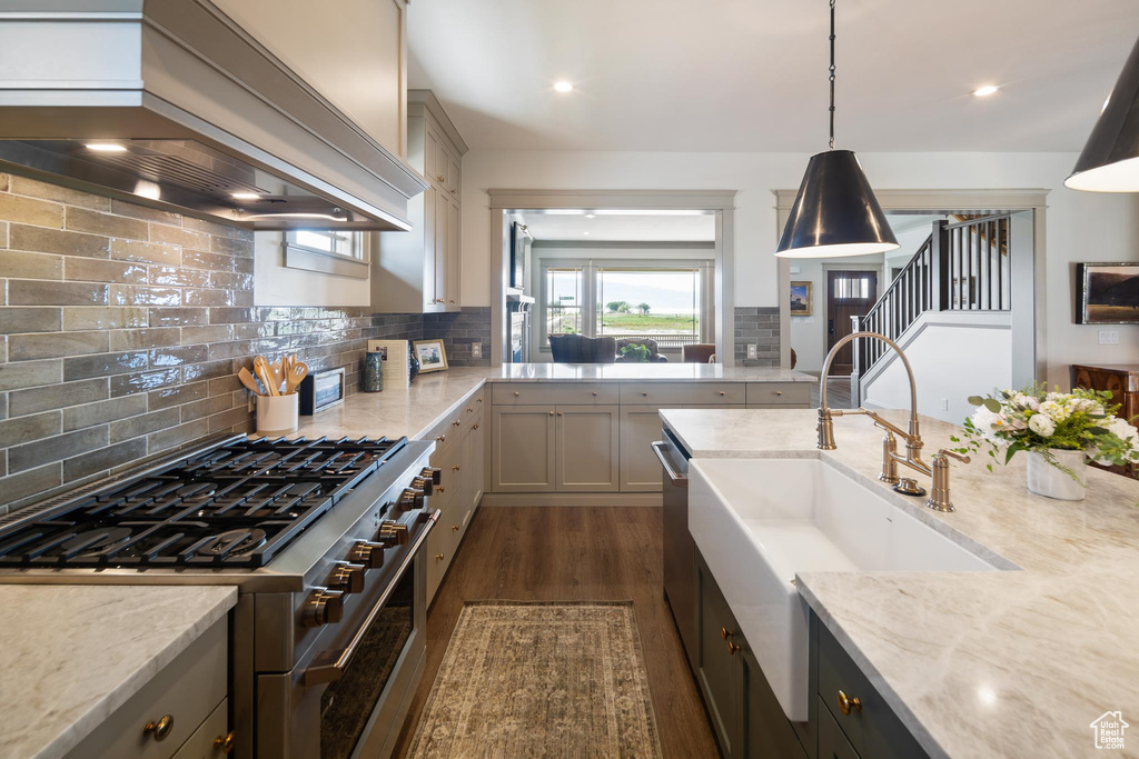 Kitchen featuring custom exhaust hood, tasteful backsplash, hanging light fixtures, and high end stove