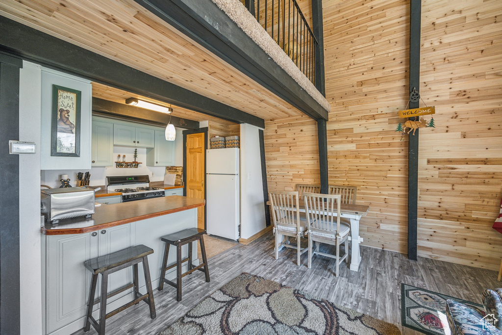 Kitchen with a breakfast bar, wood walls, light hardwood / wood-style floors, and white appliances