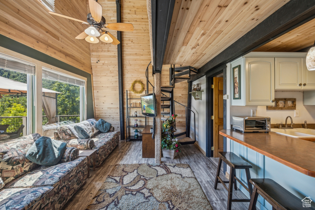 Living room featuring wood walls, sink, beam ceiling, dark wood-type flooring, and ceiling fan