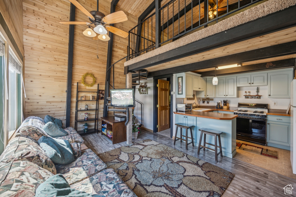 Living room with ceiling fan, wooden walls, high vaulted ceiling, and dark wood-type flooring