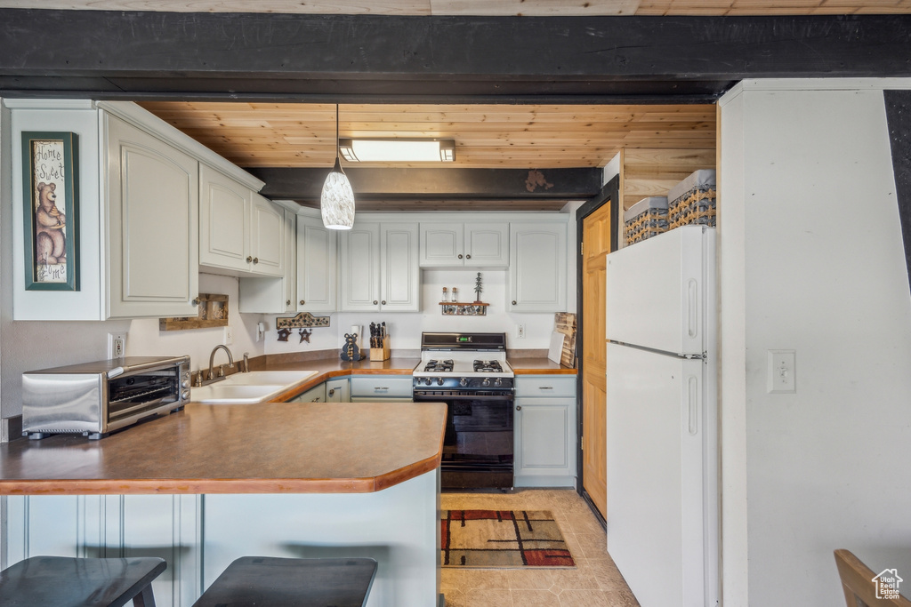 Kitchen featuring sink, decorative light fixtures, white fridge, range with gas stovetop, and kitchen peninsula