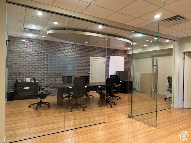 Home office featuring light hardwood / wood-style flooring, a paneled ceiling, and brick wall