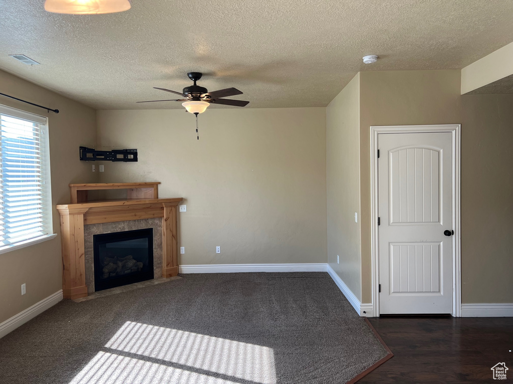 Unfurnished living room with a textured ceiling, ceiling fan, a tiled fireplace, and dark hardwood / wood-style flooring