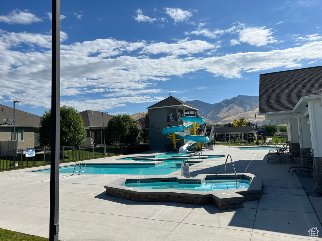 View of swimming pool featuring a mountain view, a water slide, a hot tub, and a patio