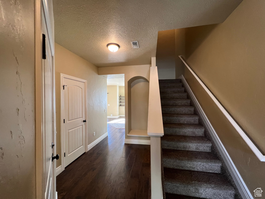 Stairway with a textured ceiling and wood-type flooring