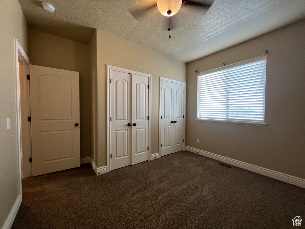 Unfurnished bedroom featuring multiple closets, ceiling fan, a textured ceiling, and dark colored carpet