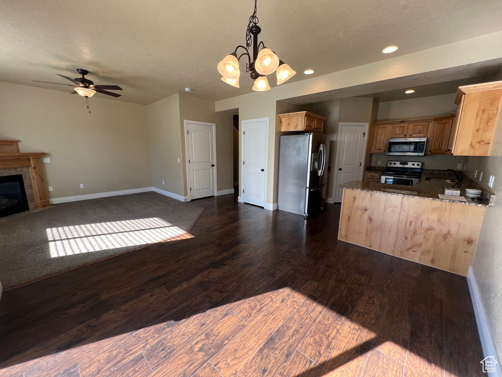 Kitchen with hanging light fixtures, ceiling fan with notable chandelier, kitchen peninsula, dark hardwood / wood-style floors, and appliances with stainless steel finishes