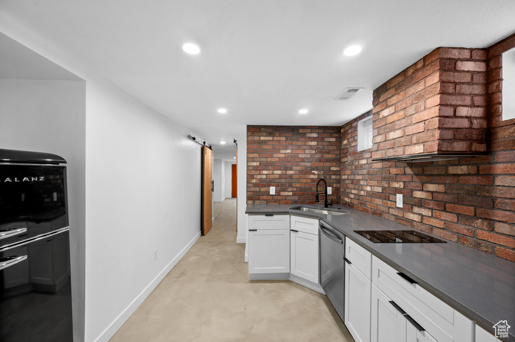 Kitchen featuring sink, dishwasher, a barn door, brick wall, and white cabinets