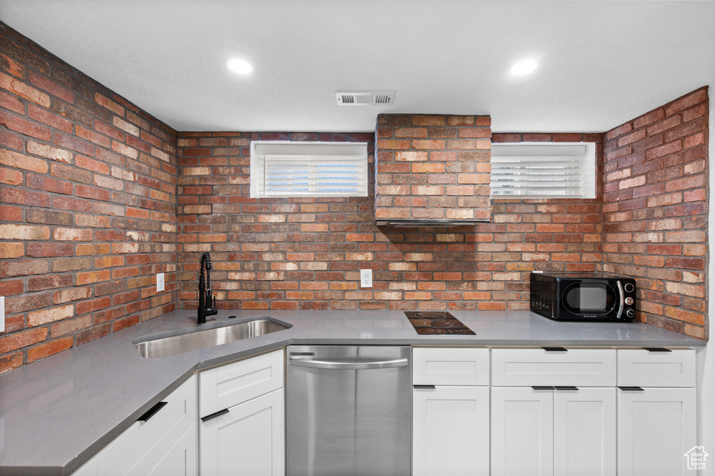 Kitchen with stainless steel dishwasher, sink, brick wall, and white cabinets