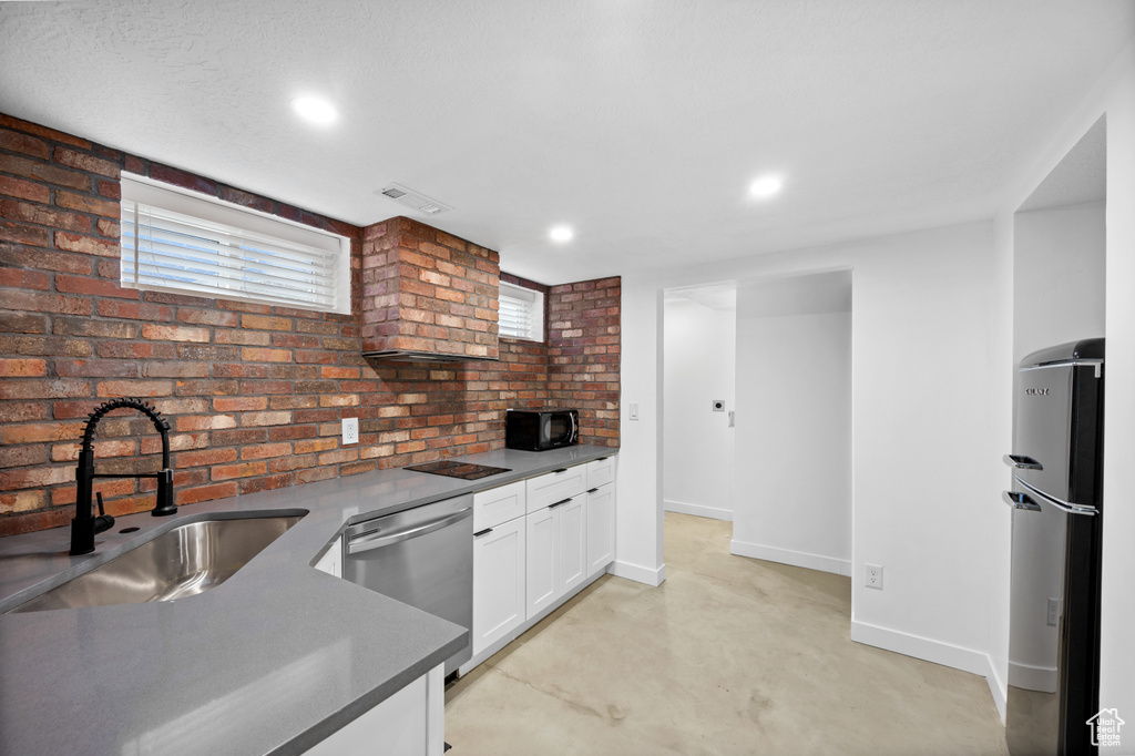 Kitchen with appliances with stainless steel finishes, sink, brick wall, plenty of natural light, and white cabinets