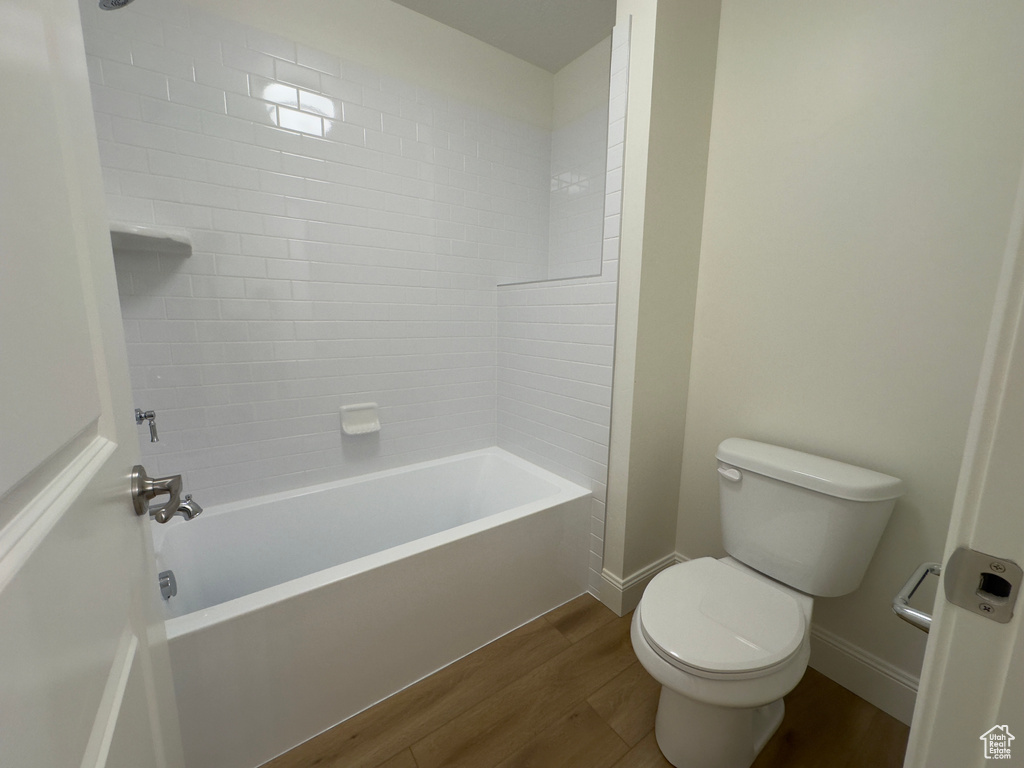 Bathroom featuring wood finished floors, toilet, baseboards, and  shower combination