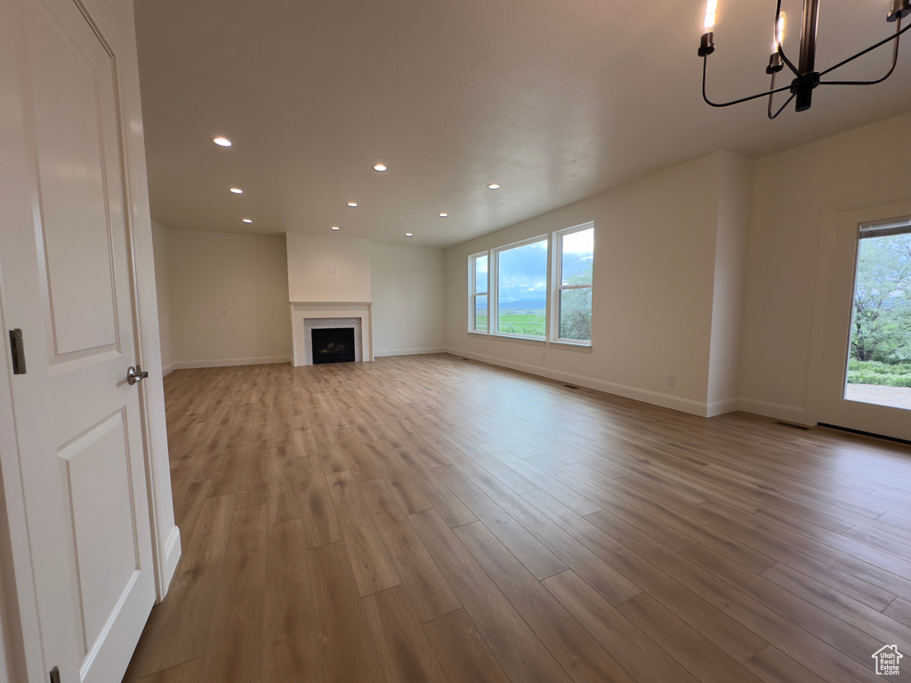 Unfurnished living room featuring wood finished floors, recessed lighting, baseboards, a chandelier, and a fireplace