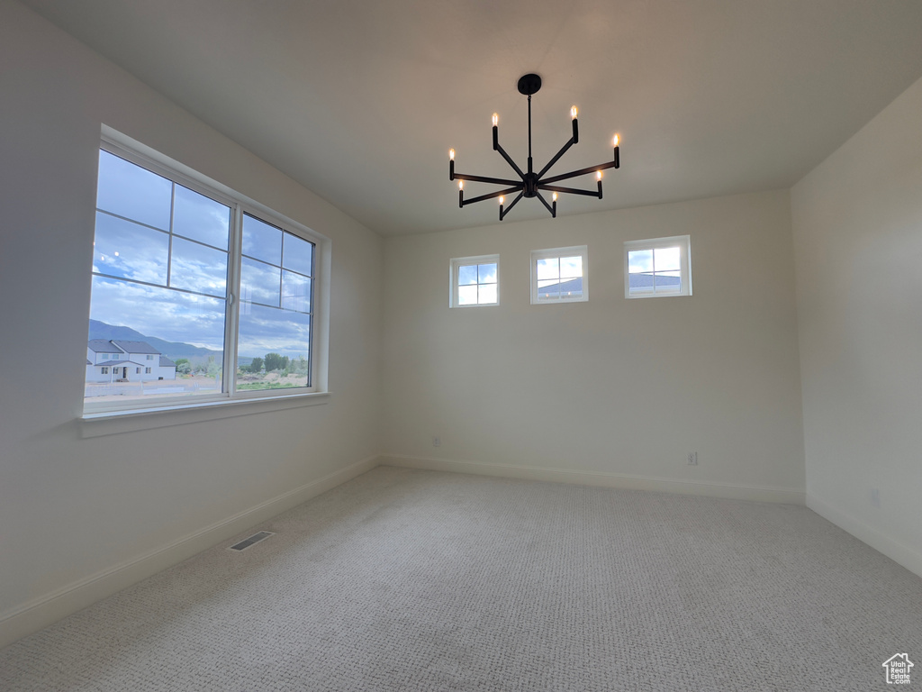 Carpeted spare room with a chandelier and baseboards