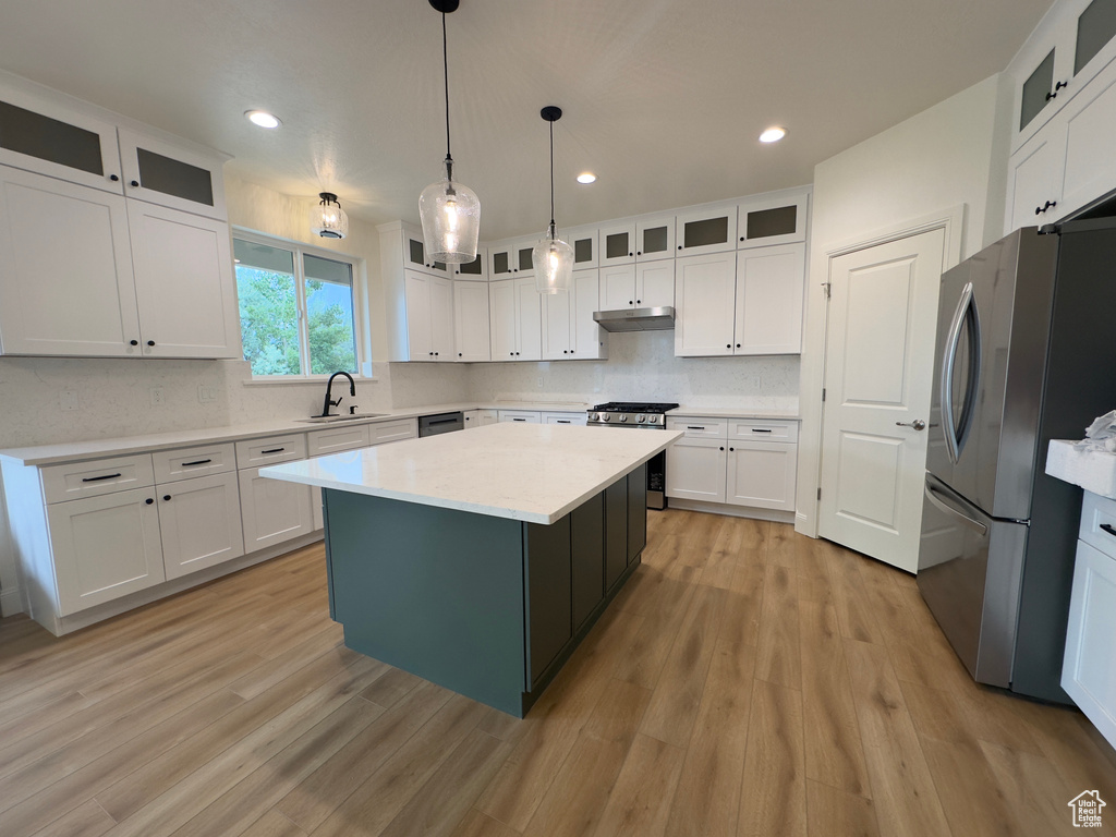 Kitchen with stainless steel appliances, under cabinet range hood, a sink, a center island, and white cabinets