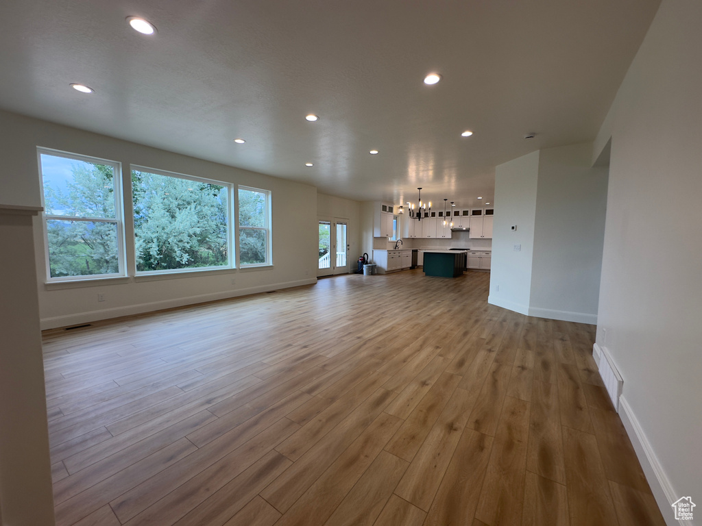 Unfurnished living room featuring a chandelier, recessed lighting, baseboards, and wood finished floors