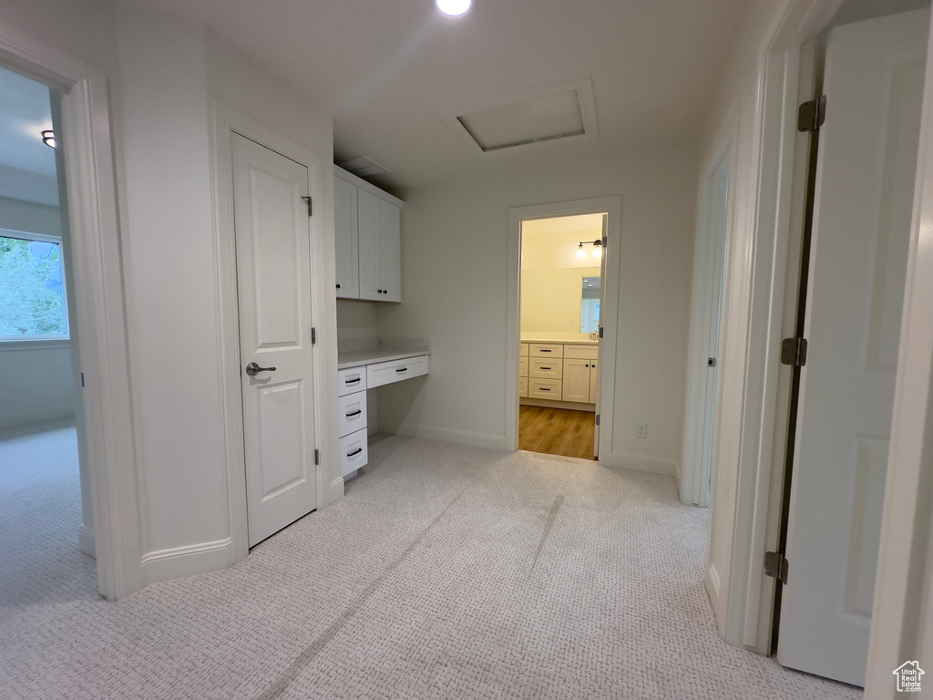 Hallway featuring light carpet, baseboards, an office area, and attic access