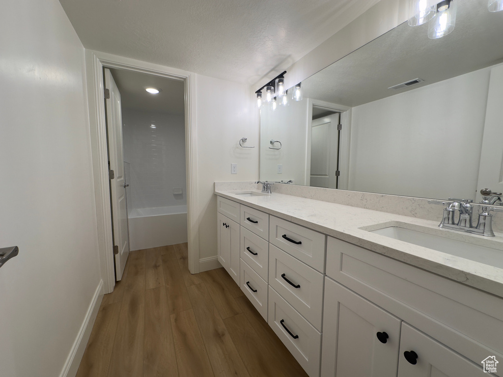 Full bathroom featuring wood finished floors, double vanity, a tub to relax in, and baseboards