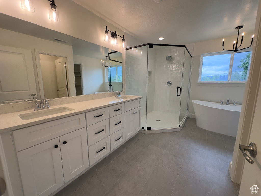 Bathroom with a chandelier, a shower stall, double vanity, a freestanding bath, and healthy amount of natural light