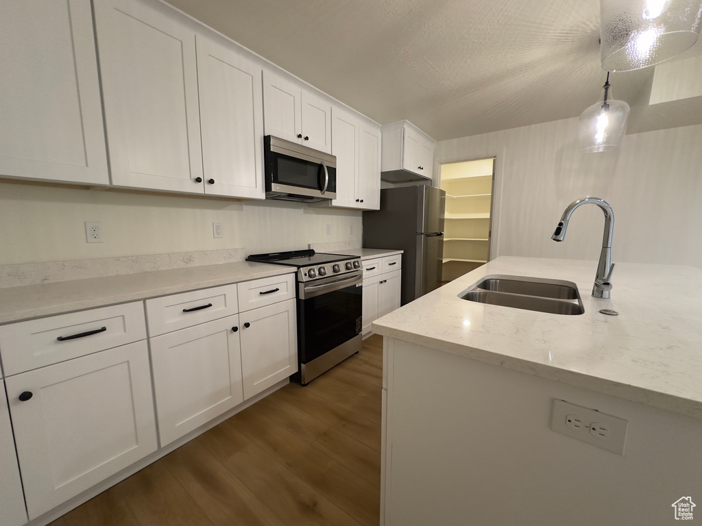 Kitchen with appliances with stainless steel finishes, a sink, dark wood-style flooring, white cabinetry, and decorative light fixtures