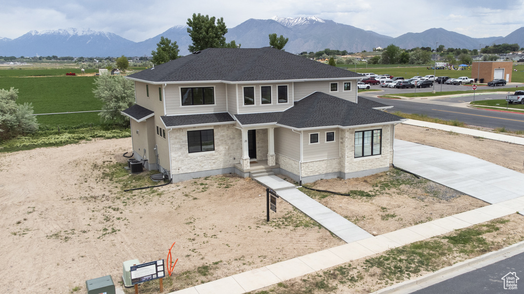 View of front of home with concrete driveway, a mountain view, a shingled roof, and stone siding