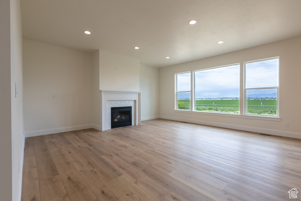 Unfurnished living room featuring recessed lighting, light wood-style floors, a glass covered fireplace, and baseboards