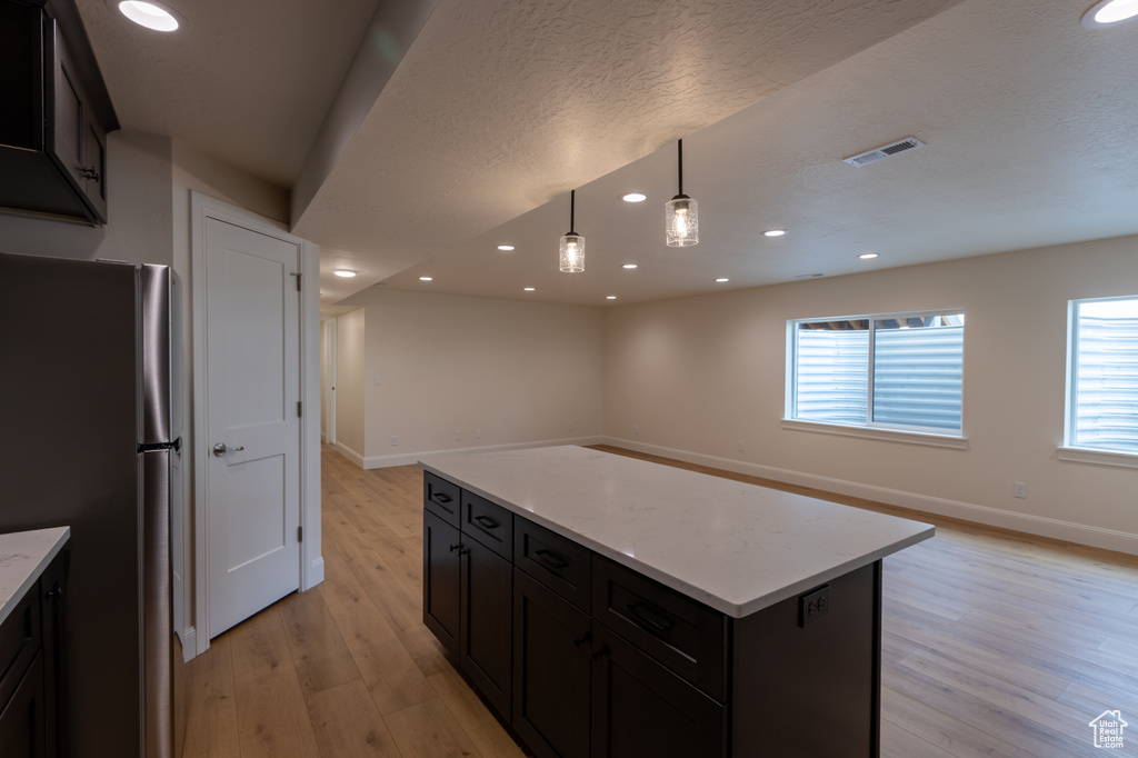 Kitchen with freestanding refrigerator, light wood finished floors, baseboards, recessed lighting, and a center island