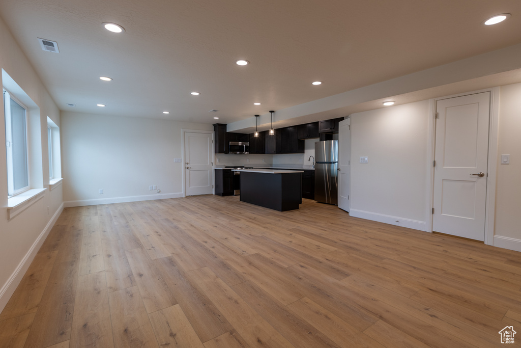 Kitchen featuring open floor plan, stainless steel appliances, light wood-style floors, a center island, and dark cabinetry
