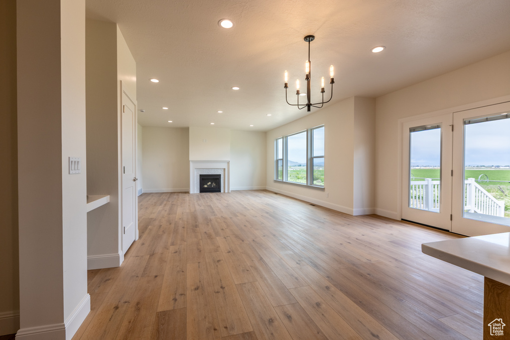 Unfurnished living room featuring light wood-type flooring, recessed lighting, a chandelier, a fireplace, and baseboards