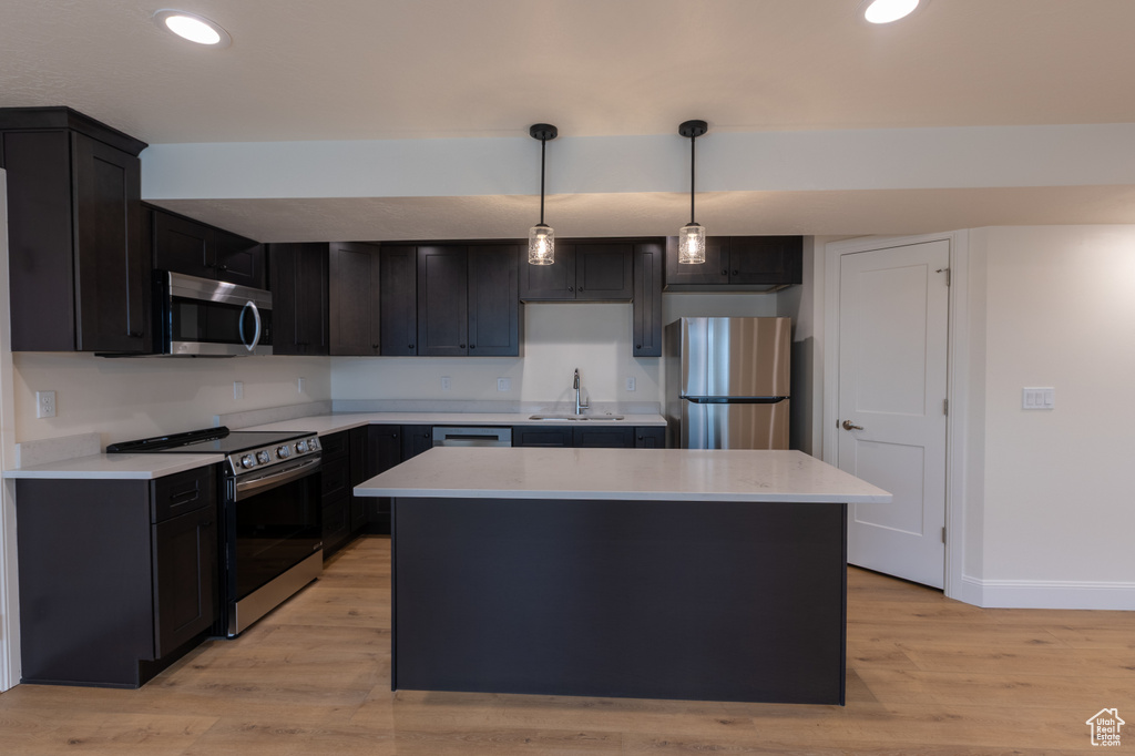 Kitchen with stainless steel appliances, a sink, light wood-style flooring, a kitchen island, and light countertops