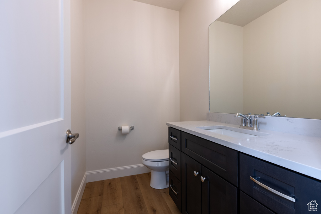 Half bathroom with wood finished floors, baseboards, toilet, and vanity