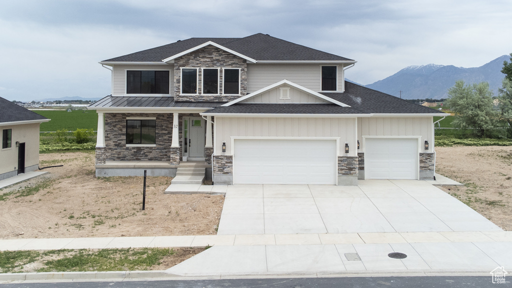 Craftsman house featuring stone siding, covered porch, an attached garage, a mountain view, and driveway