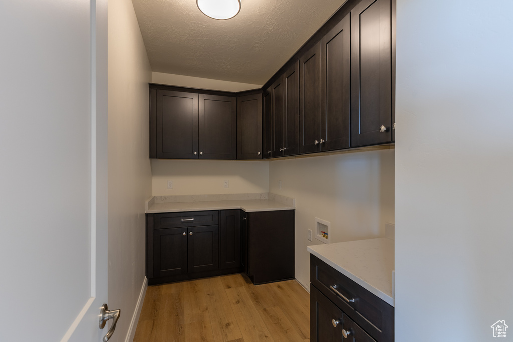 Laundry area featuring cabinet space, light wood-style flooring, washer hookup, and a textured ceiling