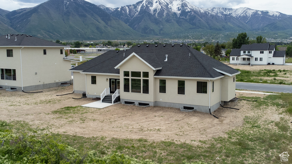 Back of house featuring a shingled roof, a mountain view, and stucco siding