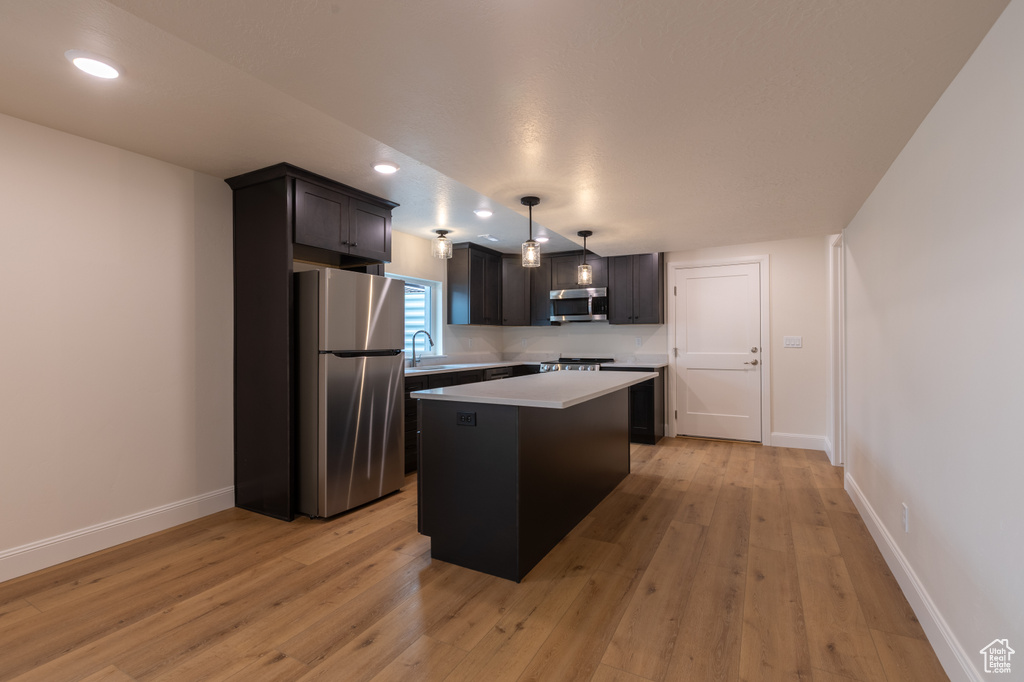 Kitchen featuring appliances with stainless steel finishes, a kitchen island, light countertops, light wood-style floors, and recessed lighting